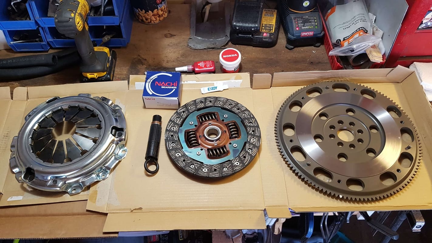 A complete clutch job laid out on a workbench: pressure plate, clutch disc, alignment tool and a lightweight flywheel on their boxes