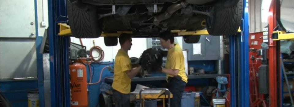 Two Clutch-Pro technicians in yellow shirts working at the bench under a lifted car